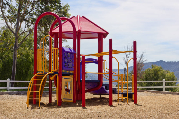 Small playground sits up on a hill with a fence and mountain range in the background. - Photo, Image