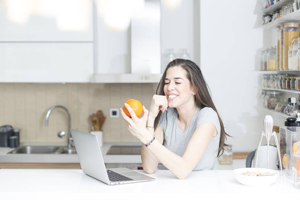 woman holding orange in front of laptop - Foto, Bild