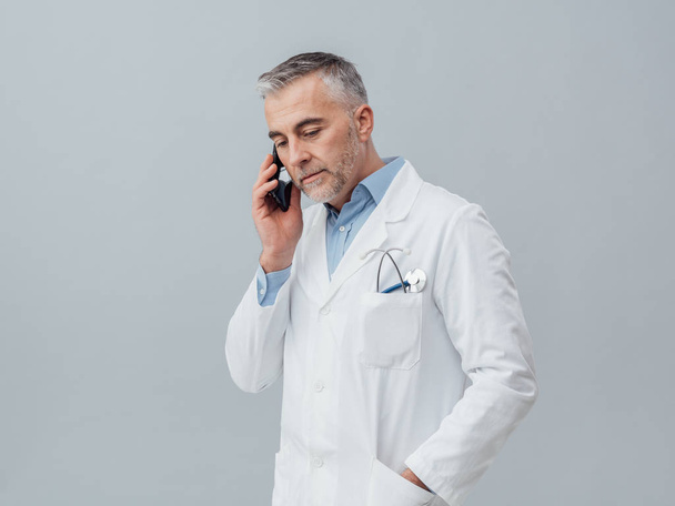 Confident mature doctor with smartphone - Foto, afbeelding