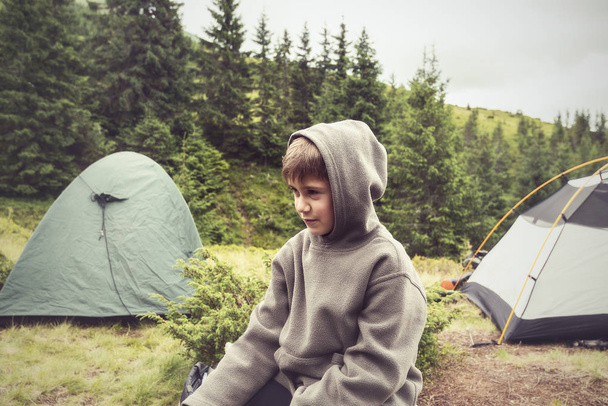 Boy with funny face, wearing hoodie, resting in camp - Foto, afbeelding