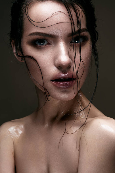A young girl with shining wet skin and wet hair on her face. Beautiful model with creative bright makeup. Beauty of the face. - Фото, изображение