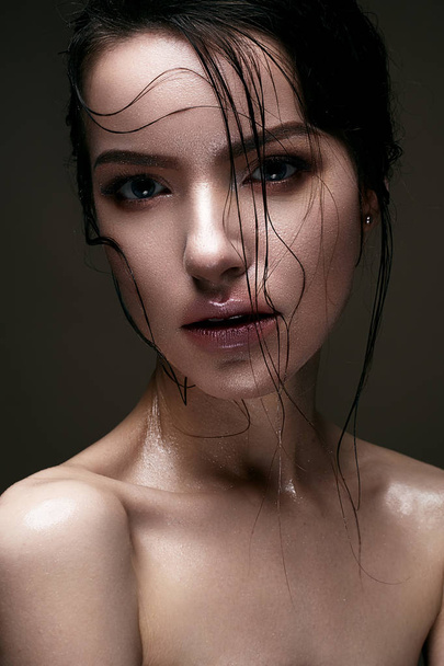 A young girl with shining wet skin and wet hair on her face. Beautiful model with creative bright makeup. Beauty of the face. - Foto, Imagen