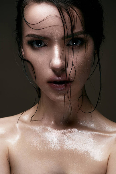 A young girl with shining wet skin and wet hair on her face. Beautiful model with creative bright makeup. Beauty of the face. - Foto, Imagem