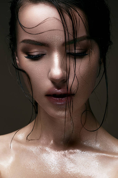 A young girl with shining wet skin and wet hair on her face. Beautiful model with creative bright makeup. Beauty of the face. - Foto, immagini