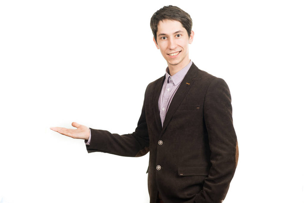 Bonito jovem empresário de terno sorrindo olhando para a câmera segurando uma palma para cima
 - Foto, Imagem