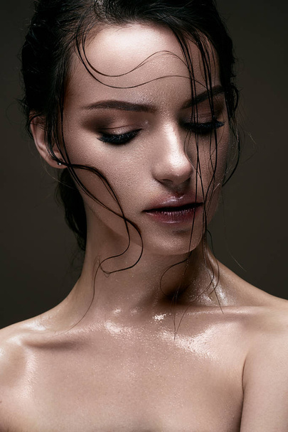 A young girl with shining wet skin and wet hair on her face. Beautiful model with creative bright makeup. Beauty of the face. - Фото, изображение