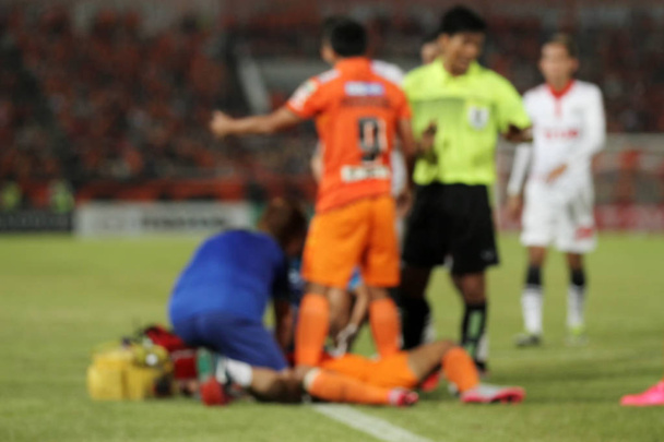 Undurchsichtige Ärzte und Schiedsrichter mit verletztem Spieler am Fußballplatz - Foto, Bild
