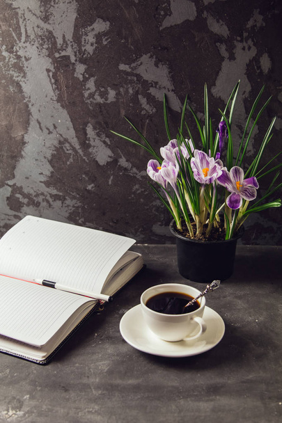 On the table is a Cup of coffee and a vase with flowers crocuses and a blank Notepad - Zdjęcie, obraz