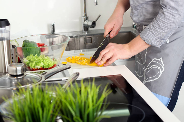 питание, семья, кулинария и люди концепция - человек рубящий паприку на разделочной доске с ножом на кухне
 - Фото, изображение