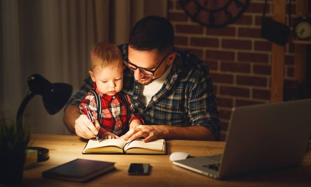 father and son baby work at home at computer in dark - 写真・画像