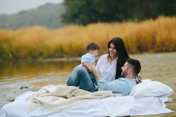 Χαρούμενη νεαρή οικογένεια χαλαρώνουν μαζί στη λίμνη - Φωτογραφία, εικόνα