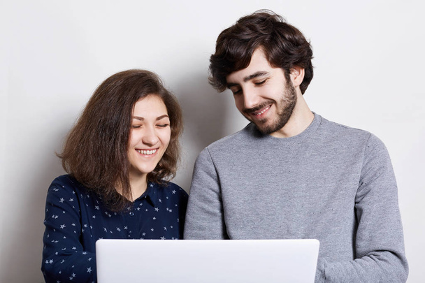 Fashionable bearded man and stylish woman standing over white background holding laptop speaking with their friends over the internet having happy expression and smile. People and technology concept - Zdjęcie, obraz