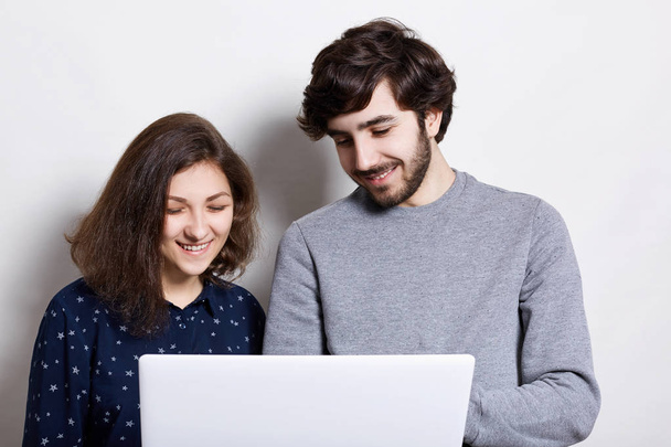 Isolated shot of young couple using laptop together. Happy modern woman and man looking into the screen of laptop watching their photos and remembering pleasant moments of their life - Фото, зображення