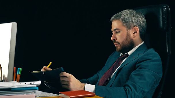 Bearded businessman checking the schedule in his personal organizer. Black background - Foto, imagen