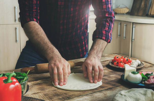 Man preparing dough for cooking homemade pizza in home kitchen - Foto, afbeelding
