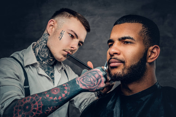 Tatuoitu parturi leikkaa parran
 - Valokuva, kuva
