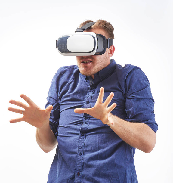 Joven excitado usando un auricular VR disfrutando de un juego interactivo con emoción de miedo y experimentando la realidad virtual aislada en un estudio de fondo blanco
 - Foto, Imagen