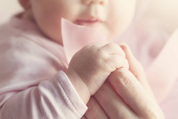 Μικρό χαριτωμένο μωρό χέρια στο χέρι της μητέρας. Ροζ φόντο.  - Φωτογραφία, εικόνα
