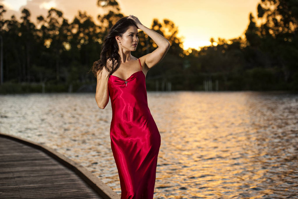 Красивая молодая женщина в садах одета в длинный шелк красный дре
 - Фото, изображение