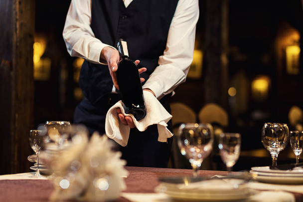 der Kellner bietet den Besuchern Wein an, der Kellner in Uniform wartet auf eine Bestellung, der Kellner mit einem weißen Handtuch auf der Hand, der selbstbewusste Kellner, ein pub.restaurant.classic.evening.european restaurant - Foto, Bild