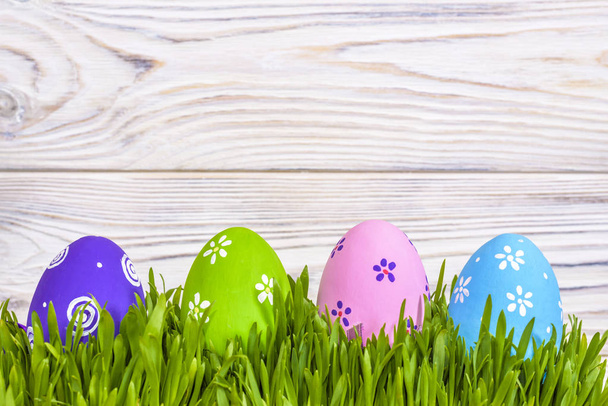 Pastel colored easter eggs in green grass over rustic wooden background. - Photo, Image