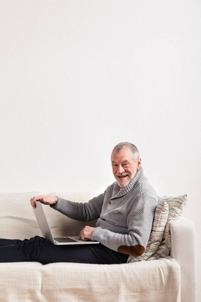 Senior férfi ül a kanapén, működő-ra laptop. - Fotó, kép