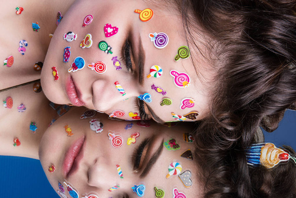 Beautiful fashion girl with luxury professional makeup and funny emoji stickers glued on the face. Young woman with cupcake in hands. - Foto, afbeelding