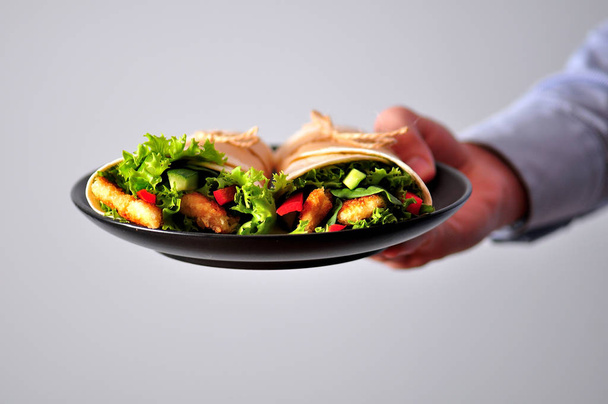 Izgara tavuk, kırmızı biber, salatalık ve marul bir gencin elinde tortilla rulo - Fotoğraf, Görsel