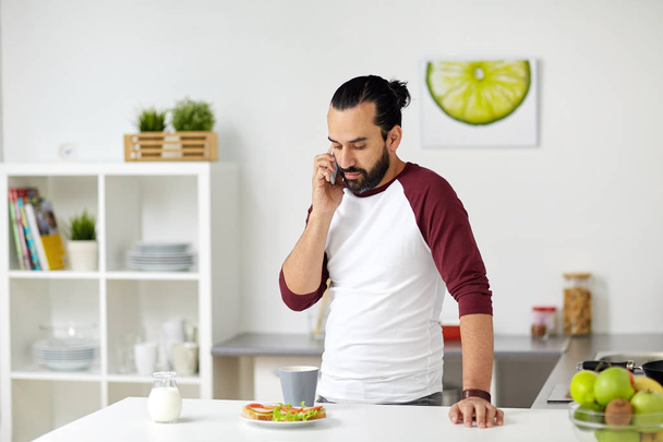mies soittaa älypuhelimeen ja syö kotona
 - Valokuva, kuva