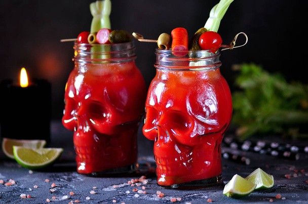 Bloody Mary cocktail in glasses-skull with celery sticks, pink salt, lime and canapes from canned vegetables. - Photo, Image
