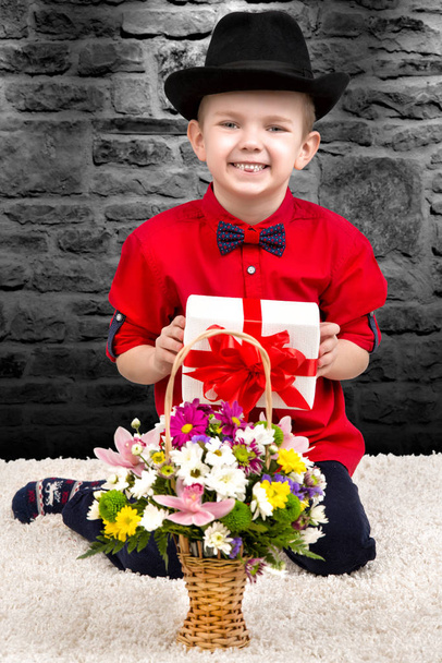 Stylish little boy in a shirt and hat with a surprise gift and a bouquet of flowers.Trendy dandy. - Fotografie, Obrázek