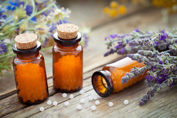 Bottles of homeopathic globules and healing herbs on wooden board. - 写真・画像