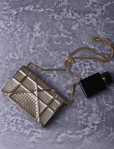 маленька жіноча металізована срібна сумка з металевим ланцюгом біля парфумів
 - Фото, зображення