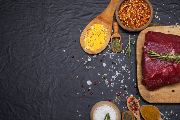 Raw beef steak on a cutting board with rosemary and spices. - Foto, afbeelding