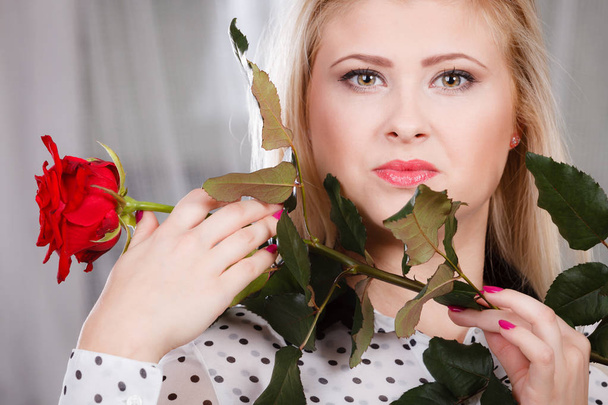 woman holding red rose near face looking melancholic - Foto, afbeelding