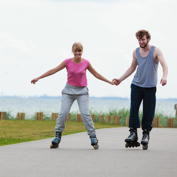 Young couple holding hands while rollerblading - Valokuva, kuva