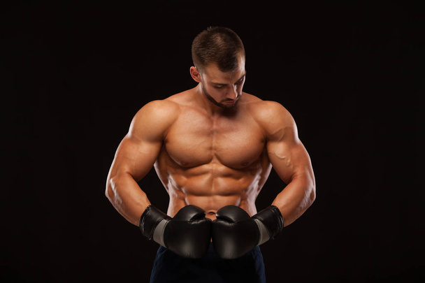 Muscular young man with perfect Torso with six pack abs, in boxing gloves is showing the different movements and strikes isolated on black background with copyspace - Fotografie, Obrázek
