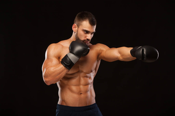 Muscular young man with perfect Torso with six pack abs, in boxing gloves is showing the different movements and strikes isolated on black background with copyspace - Photo, image