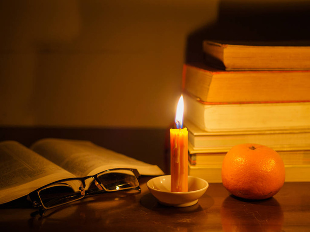 открытая книга со стопкой старой рваной книги на деревянном столе зажжённой свечи и стаканов
 - Фото, изображение