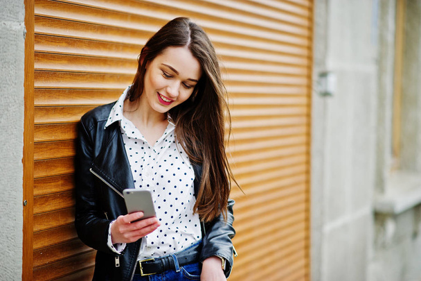 Portrét stylový mladé dívky nosí na koženou bundu s mobil - Fotografie, Obrázek