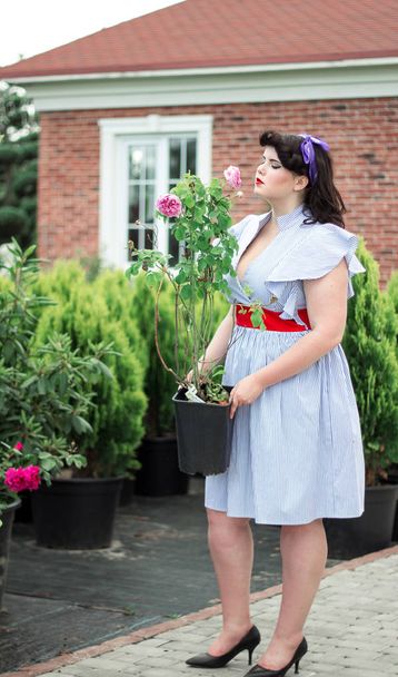 Girll sniffing τριαντάφυλλο σε γλάστρα κοντά στο σπίτι. - Φωτογραφία, εικόνα