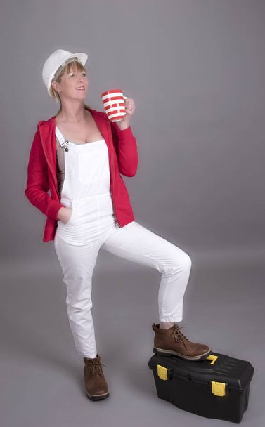 Female worker wearing dungarees drinking from a mug - Foto, Imagen