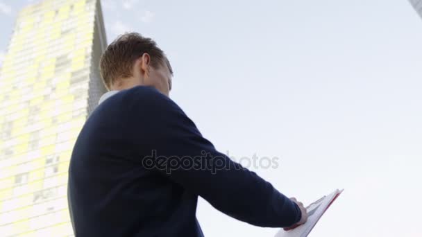 man taking notes in folder on the city street at urban modern lanscape and lookinf at sides - Πλάνα, βίντεο