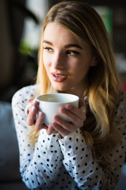Portrait of young gorgeous female drinking tea and thoughtfully looking out of the coffee shop window while enjoying her leisure time alone - Foto, Imagen
