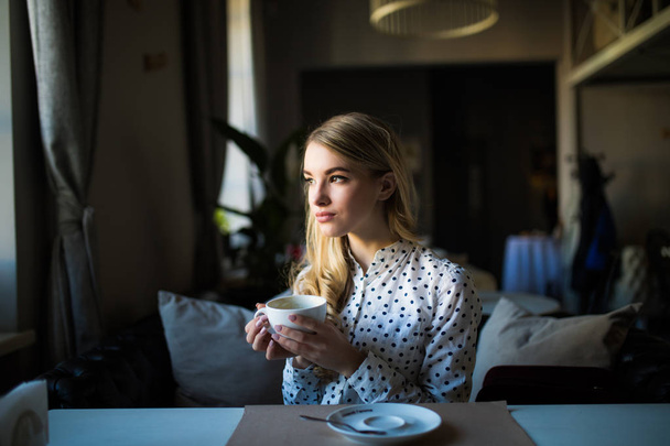 Jonge blonde vrouw genieten van koffie tijd in café - Foto, afbeelding