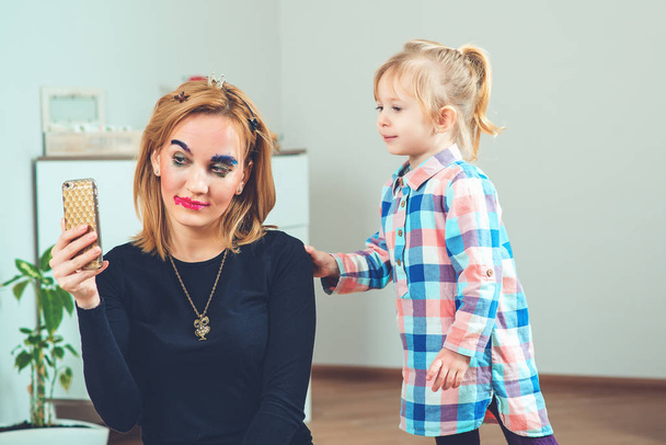 Cute little girl are doing makeup and hairstyle for her beautiful mother. Toned. - Zdjęcie, obraz