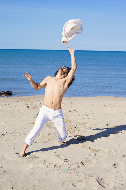 Cool man throwing shirt in the air in front of the ocean - Photo, Image