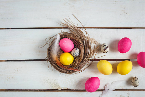Easter background with yellow and pink eggs . Top view with copy space . Easter eggs in nest on rustic wooden planks - Fotografie, Obrázek