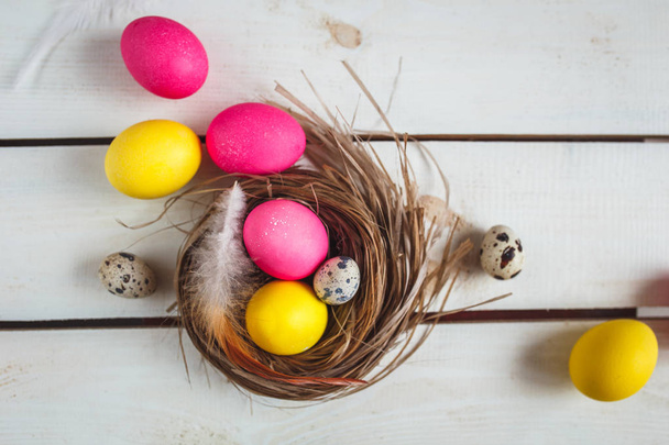 Easter background with yellow and pink eggs . Top view with copy space . Easter eggs in nest on rustic wooden planks - Foto, immagini