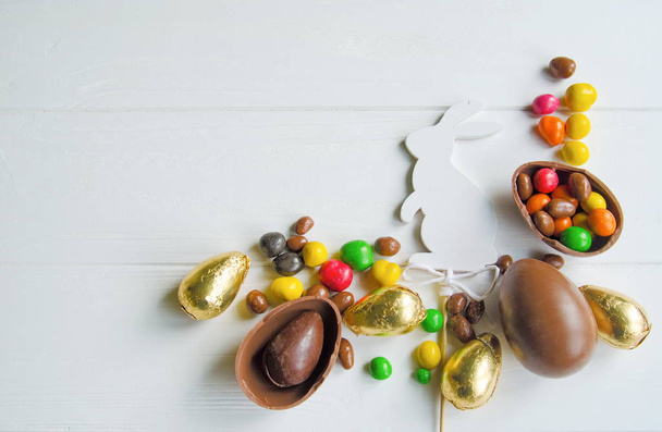 Coniglietto di Pasqua bianco con uova di cioccolato e caramelle su sfondo di legno bianco
 - Foto, immagini